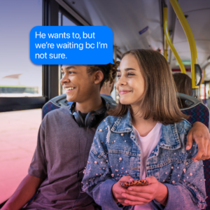 A teenage African American boy puts his arm around the shoulders of a teenage Caucasian girl as they sit on the bus, both are smiling and looking out the window, with a thought bubble that says 'He wants to, but we're waiting bc I'm not sure.'